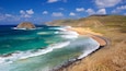 Un paisaje costero con aguas turquesas cristalinas, una playa arenosa y un promontorio rocoso.