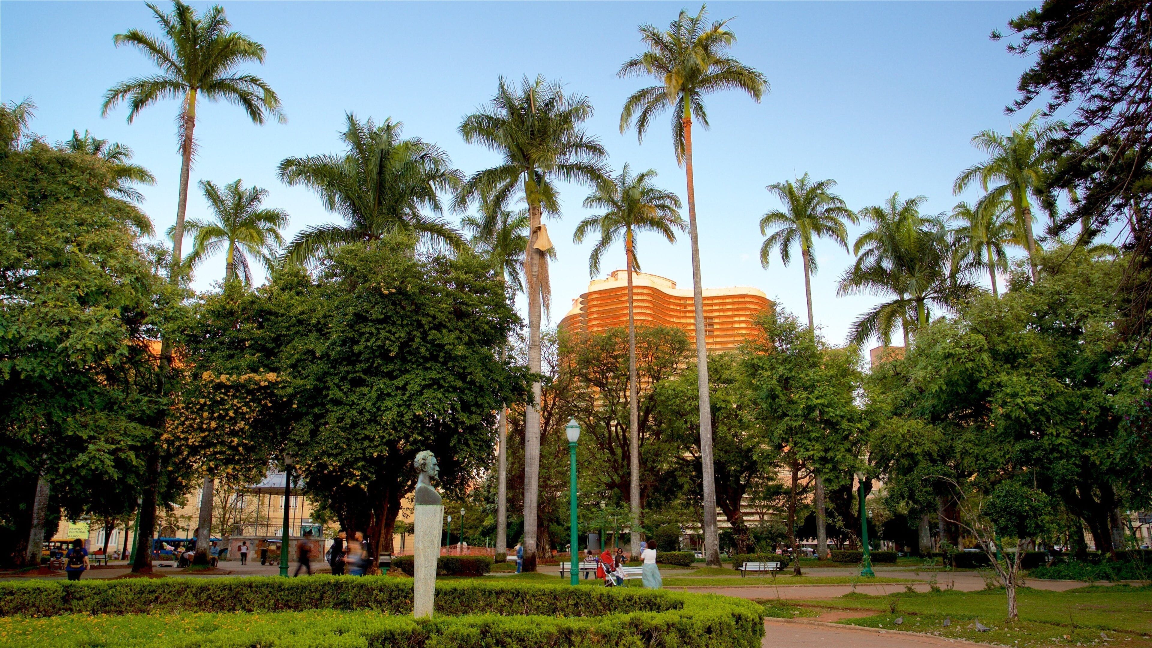 A park with palm trees, a statue, and a large building in the background.