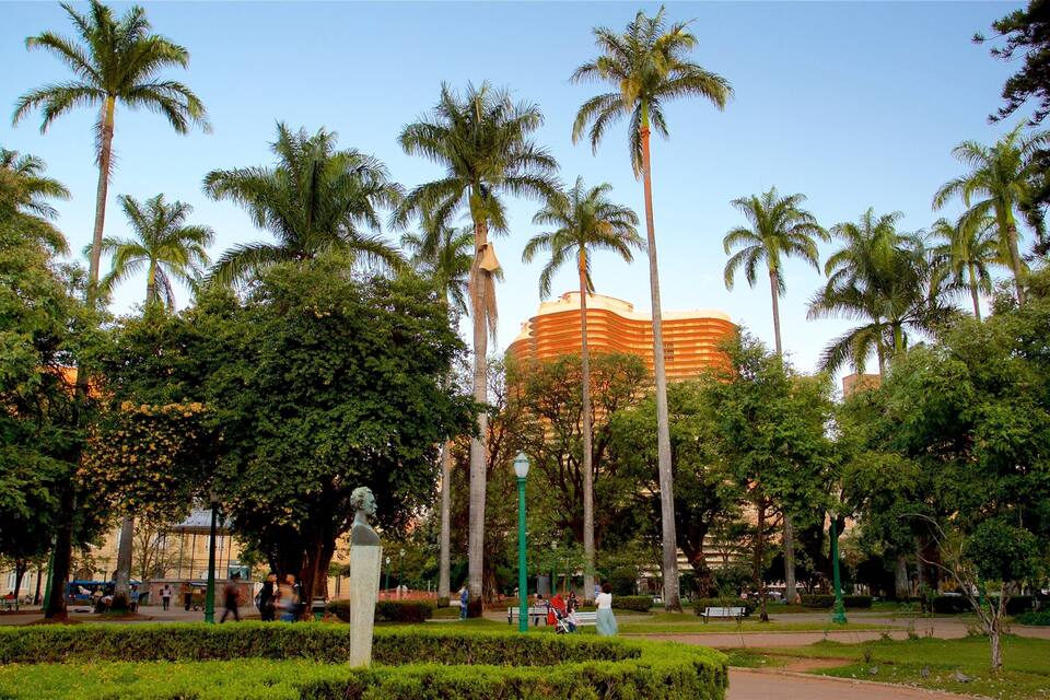 A park with palm trees, a statue, and a large building in the background.