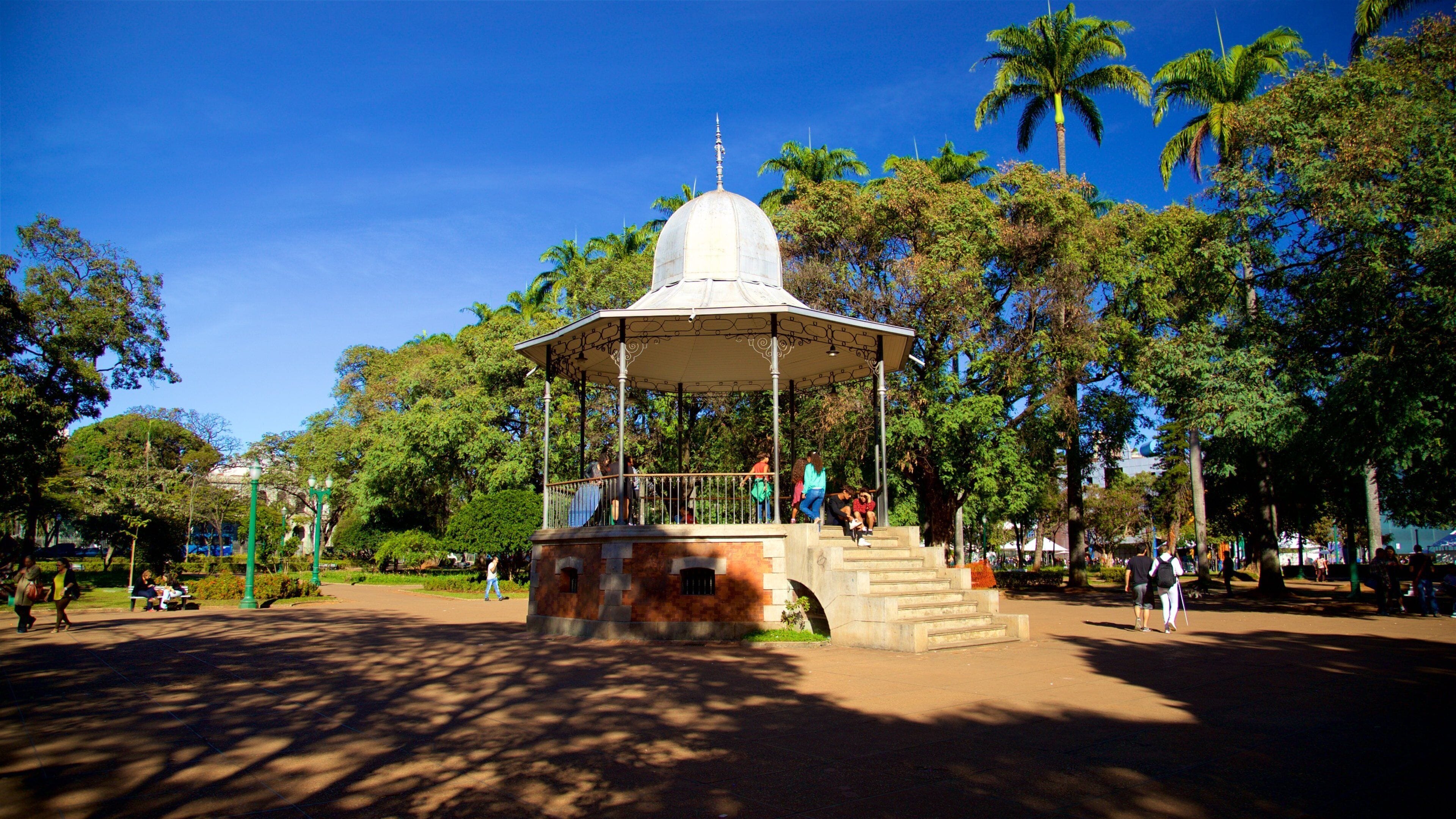 A gazebo in a park with palm trees and people around.