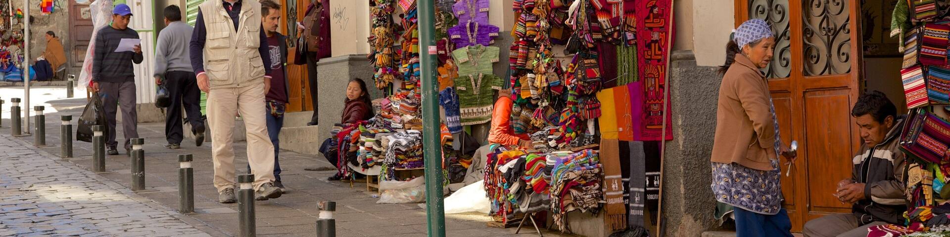 A street market with colorful textiles and handicrafts displayed outside shops.