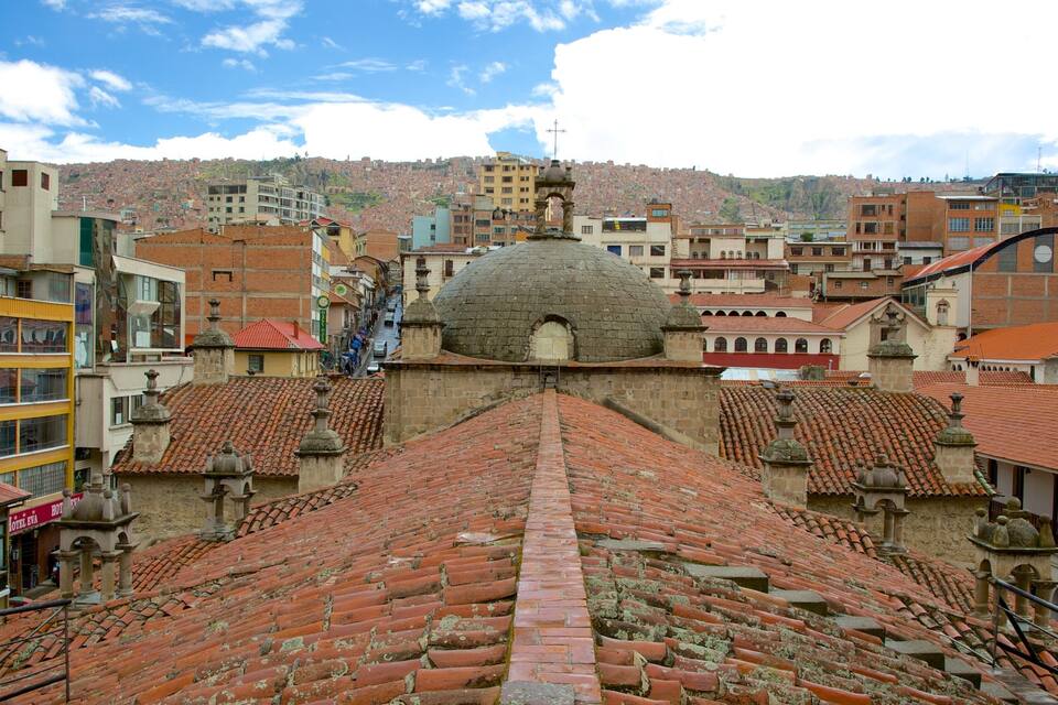 Un paisaje urbano histórico con edificios de tejados de teja rojiza, una estructura cúpula destacada y una colina al fondo.