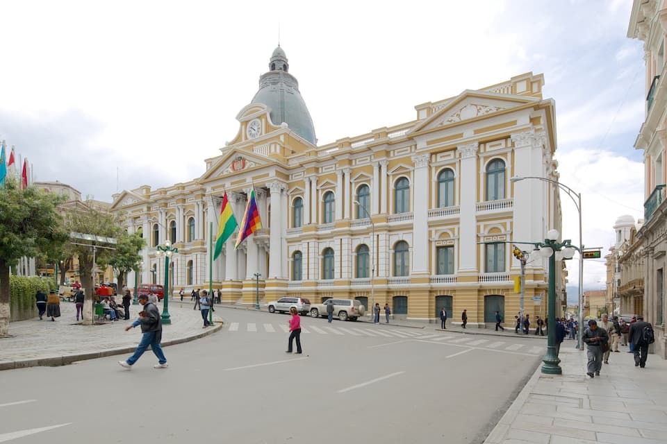 A historic building with a prominent dome and columns, surrounded by pedestrians and flags.