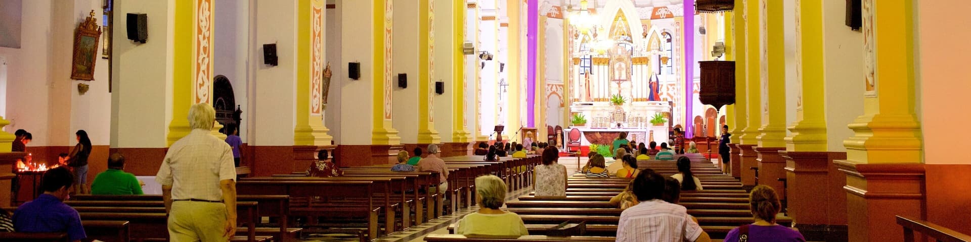 An interior of a church with high arched ceilings, wooden pews, and a central altar.