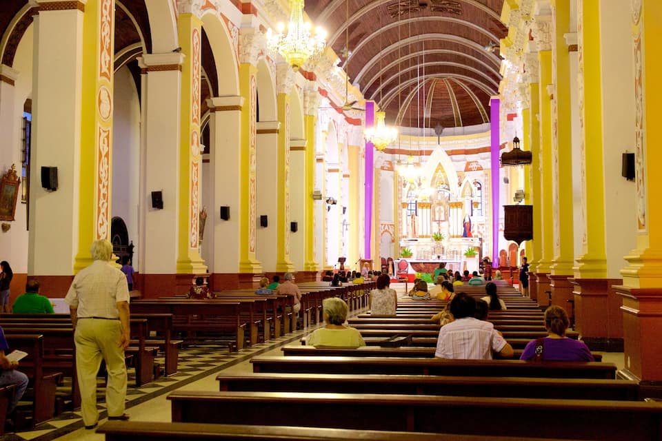 An interior of a church with high arched ceilings, wooden pews, and a central altar.