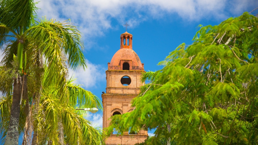 Una torre de ladrillo histórica con cúpula y campana, rodeada de exuberantes palmeras.