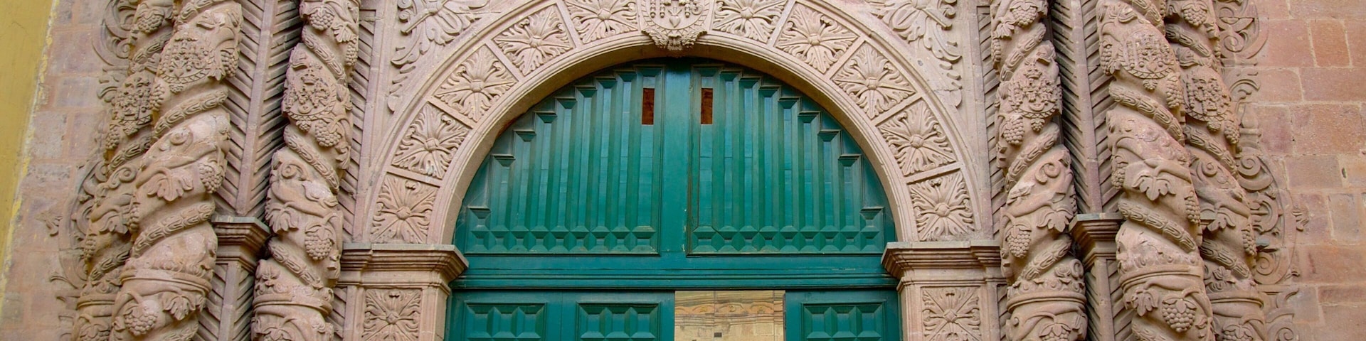Uma porta verde em arco com esculturas detalhadas e fachada de pedra.