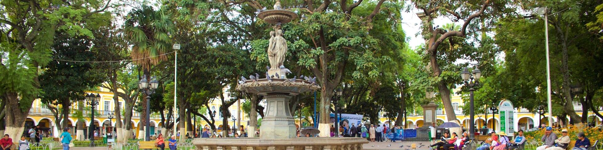 A park with a central fountain, surrounded by trees and benches.