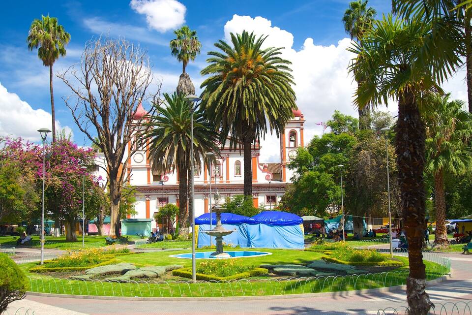 A well-maintained garden with a fountain, palm trees, and a historic building with a clock tower.