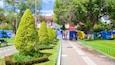 Un parco curato con siepi ordinate, un vialetto lastricato e un edificio rosso con finestre ad arco sullo sfondo.