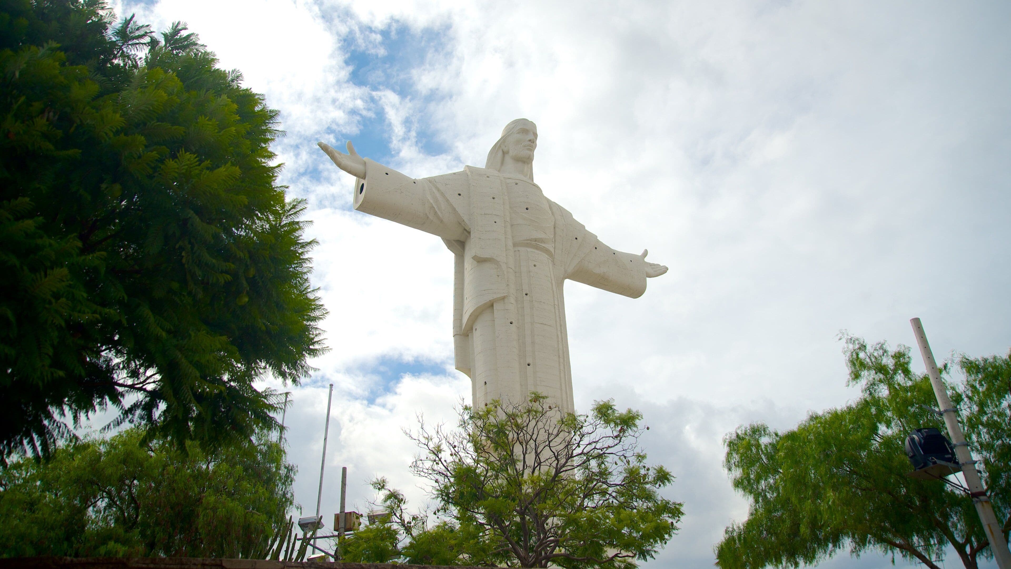 A large white statue with outstretched arms, surrounded by trees and a cloudy sky.