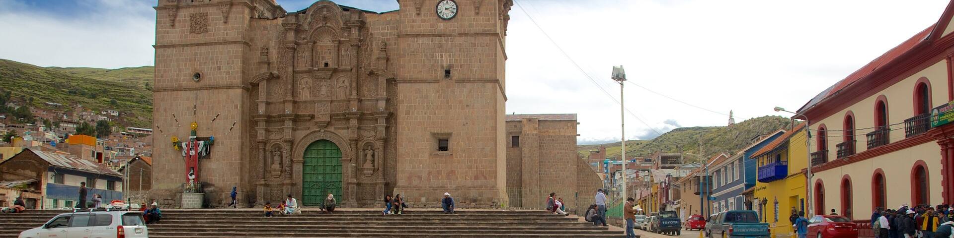 Una catedral histórica con dos torres de campanas y un reloj, rodeada de edificios coloridos y un paso de peatones.