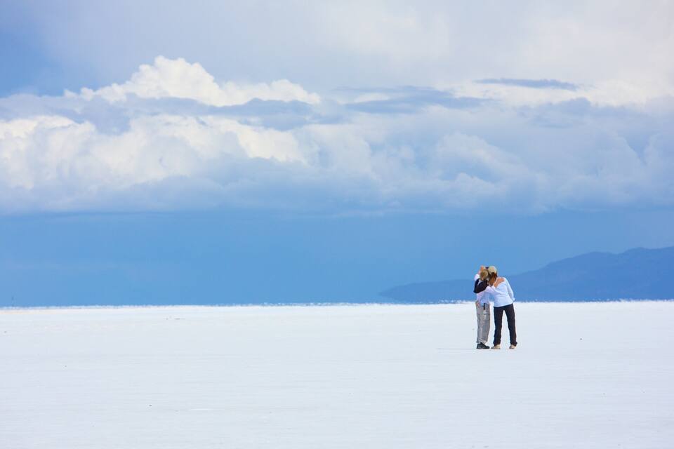 Two people embracing in a vast, flat, white landscape with a clear sky and distant mountains.