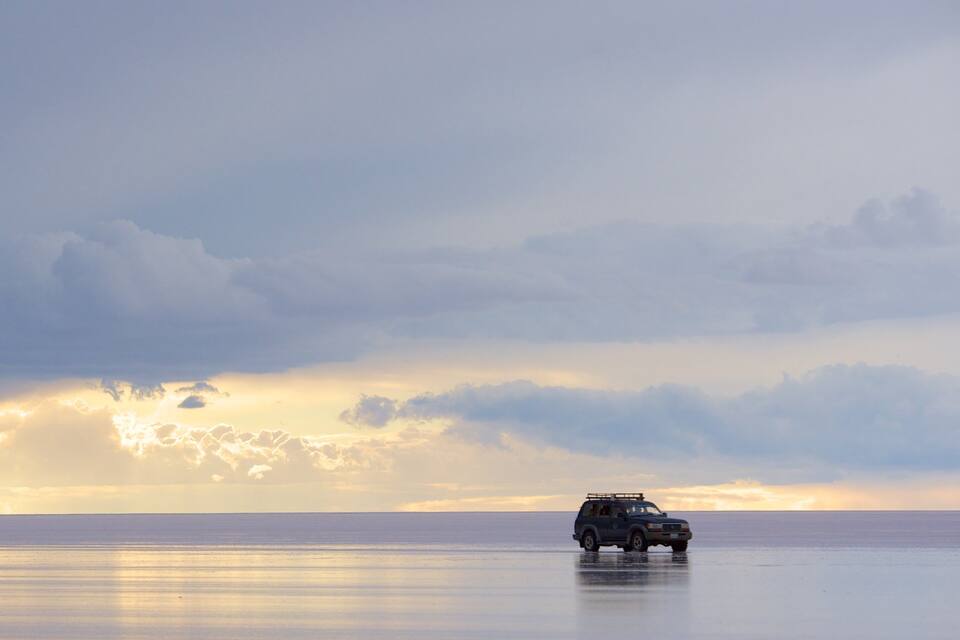 A vehicle on a reflective water surface with a cloudy sky and a sunset.