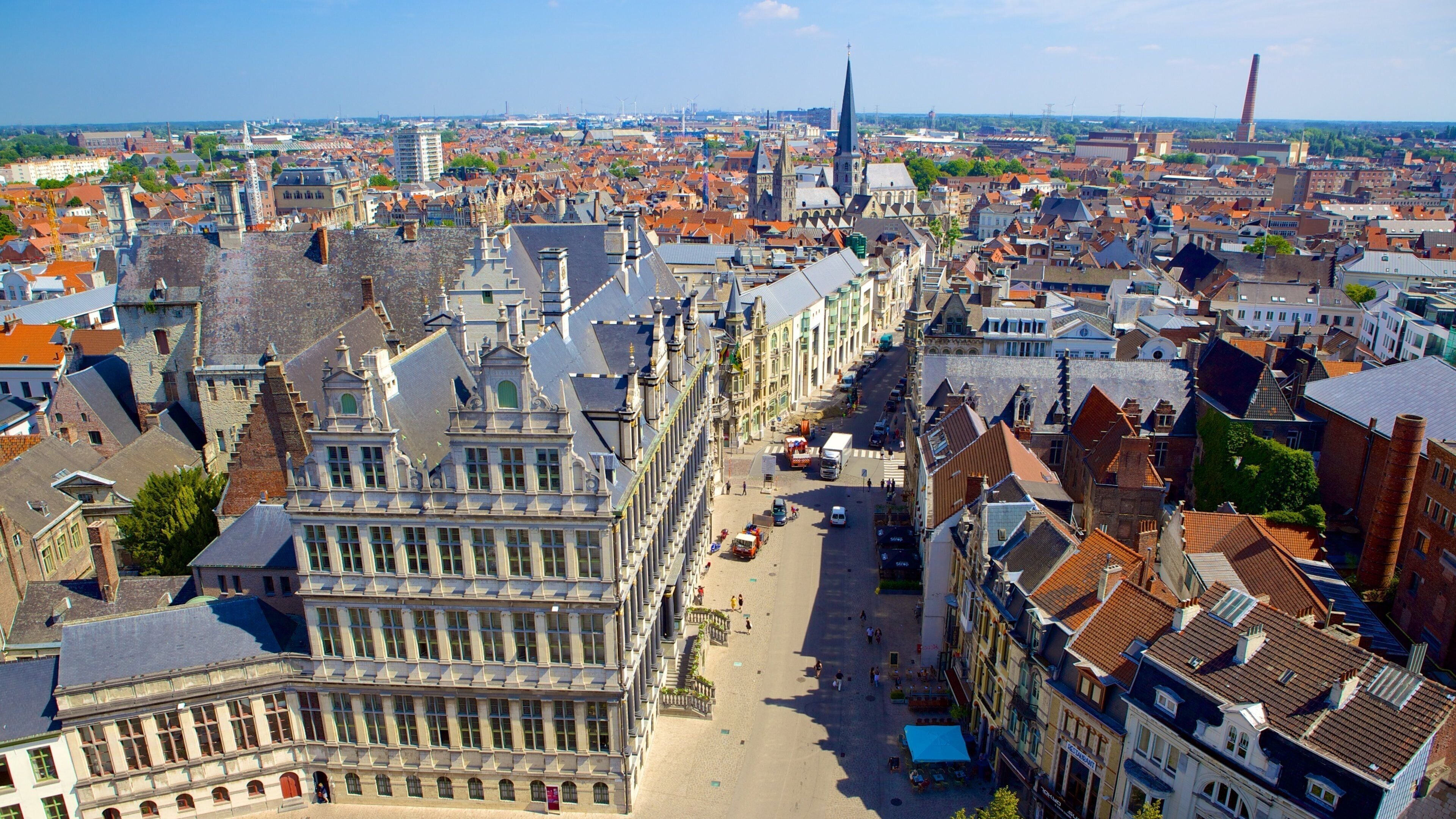 A historic European cityscape with prominent Gothic architecture, a wide street, and a distant wind turbine.