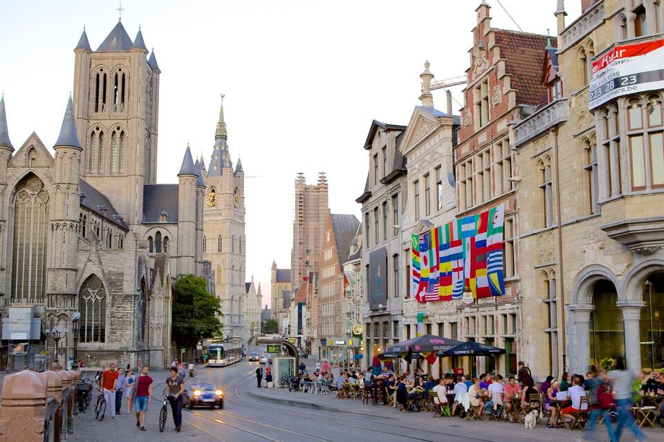 A historic cathedral with tall spires, a bustling street with cafes, and a tram in the background.