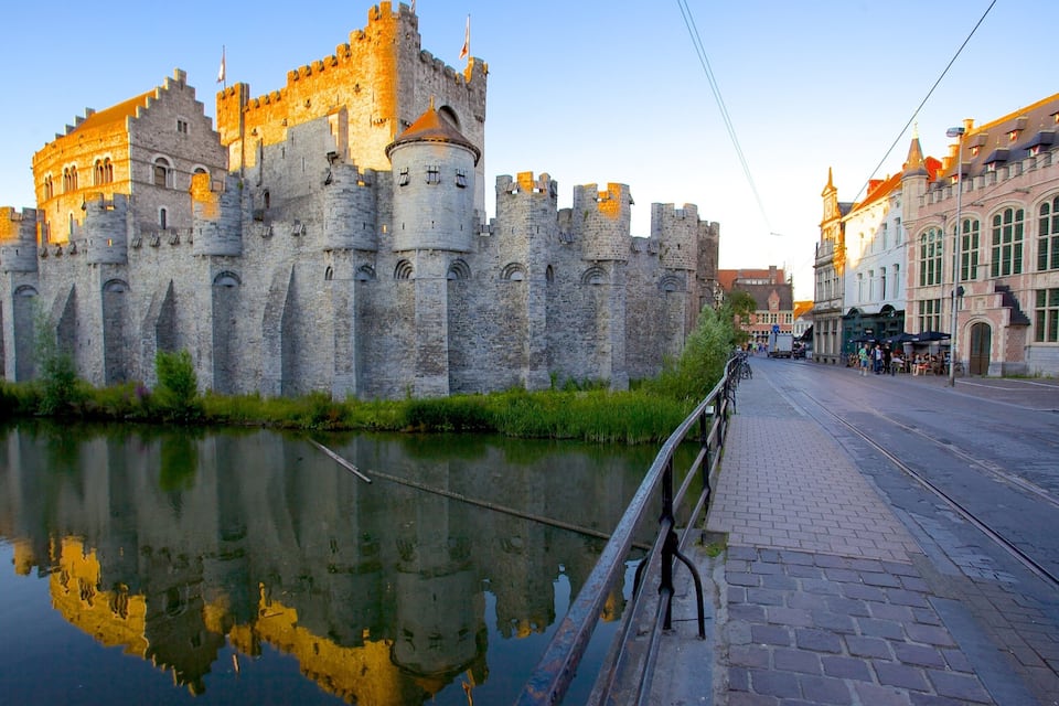 A historic castle with a moat, a bridge, and a canal reflecting the structure.