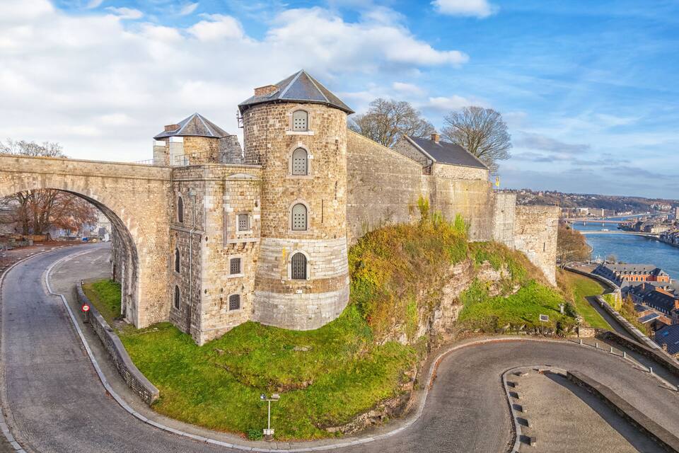 Un château de pierre historique, avec un pont, une rivière et une vue sur la ville en arrière-plan.