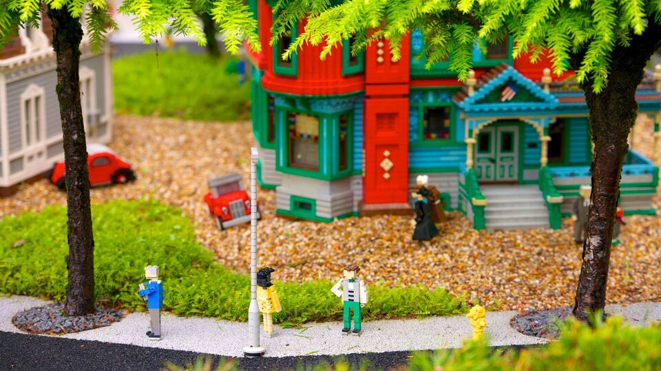 A LEGO scene with a red and green house, a red car, and LEGO figures on a gravel path.