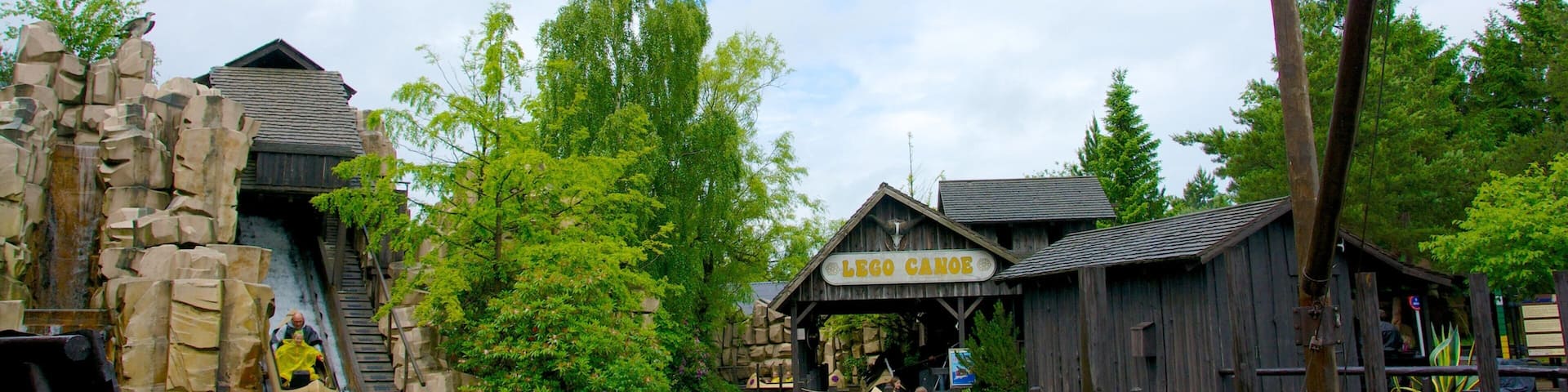 A wooden water ride with a LEGO-themed sign, surrounded by greenery and a cloudy sky.