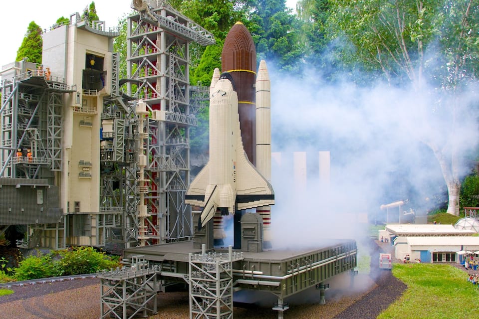 Modelo detallado de una plataforma de lanzamiento del transbordador espacial, con un transbordador en la torre de lanzamiento, rodeado de vegetación y una pequeña multitud.