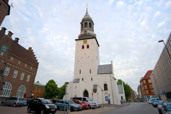 Eine historische Kirche mit einem hohen Glockenturm, umgeben von modernen Gebäuden und parkenden Autos.