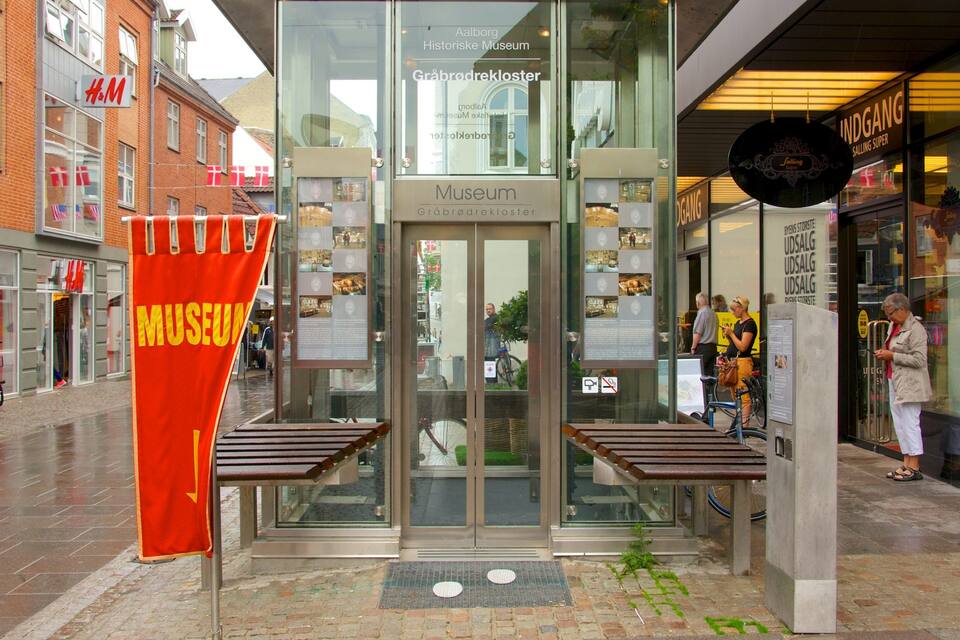 The entrance to the Gråbrødrekloster Museum with a red banner and wooden benches in front.