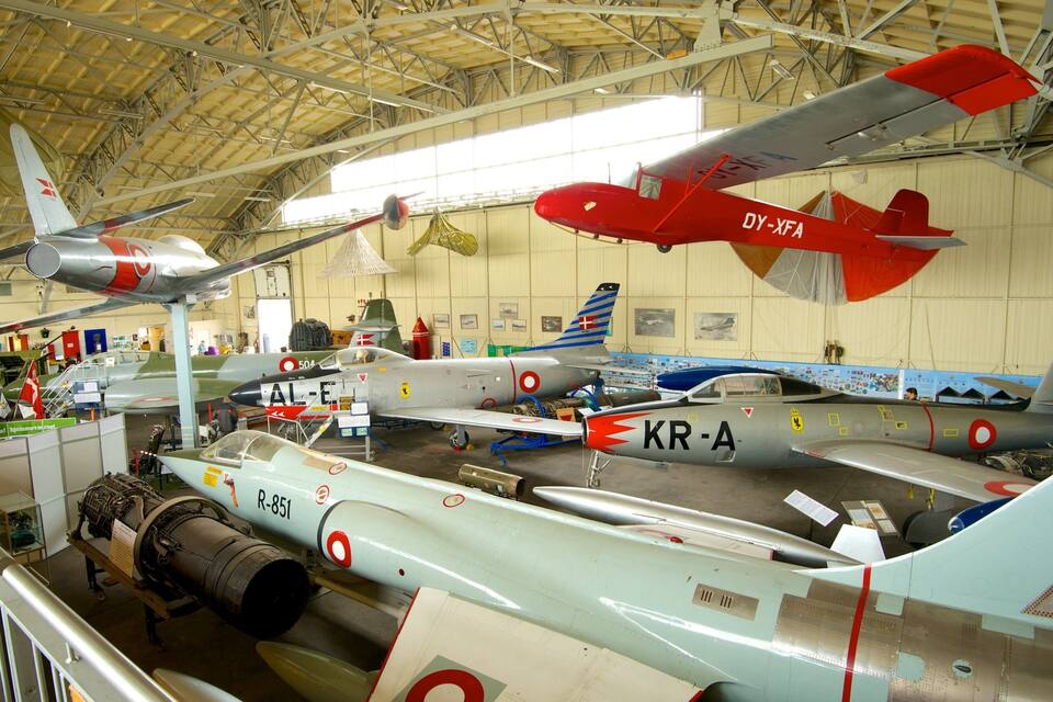 Una col·lecció d'aeronaus militars antigues exposades a l'interior, incloent un avió vermell amb el número de registre DY-XFA i un avió platejat amb el número de registre KR-A.
