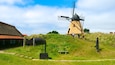 Eine traditionelle Windmühle auf einem grasbewachsen Hügel mit einem Gebäude mit Strohdach in der Nähe.