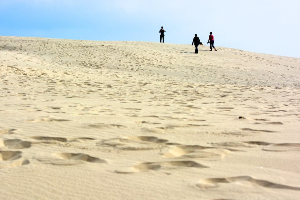 A sandy hill with footprints and three people walking.