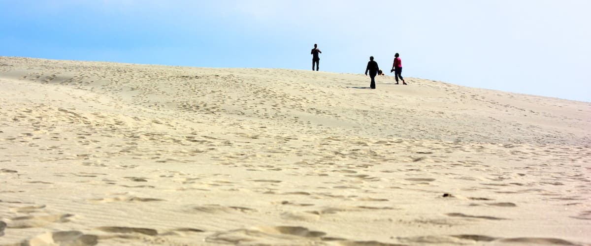 A sandy hill with footprints and three people walking.