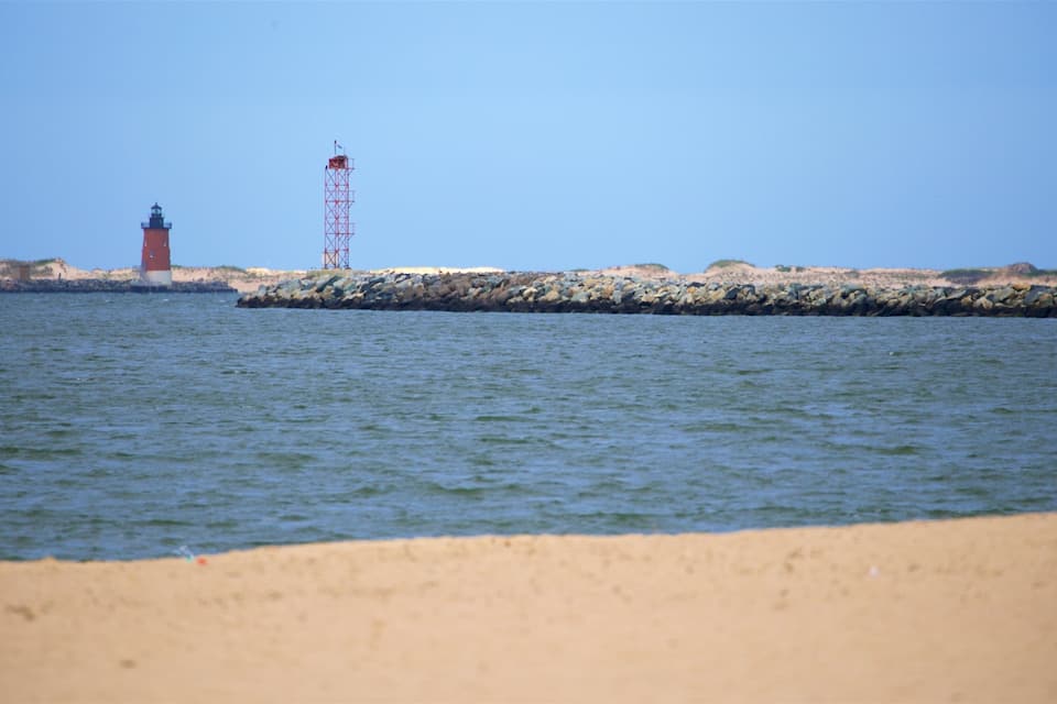 Um farol e uma torre vermelha numa costa rochosa com águas calmas.