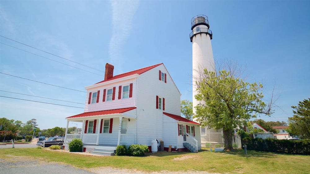 A white house with red trim and a lighthouse in the background.