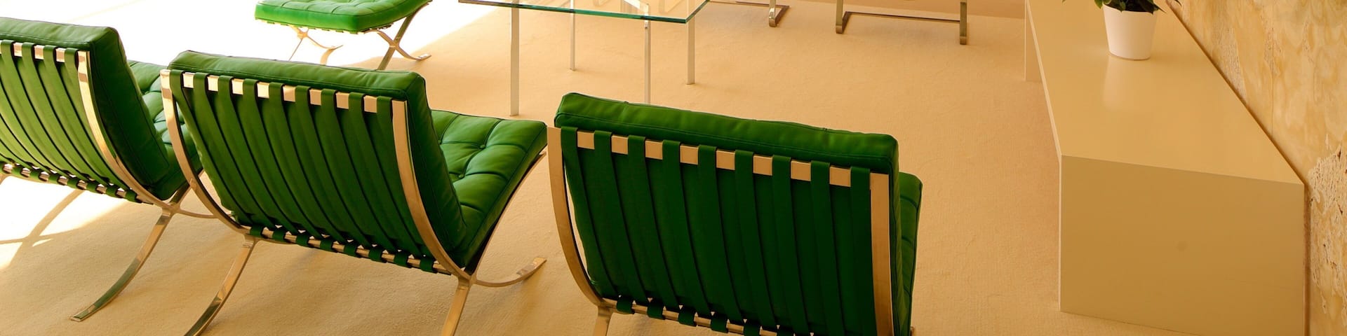 A modern living room with green chairs, a glass coffee table, and a view of a balcony with a railing.