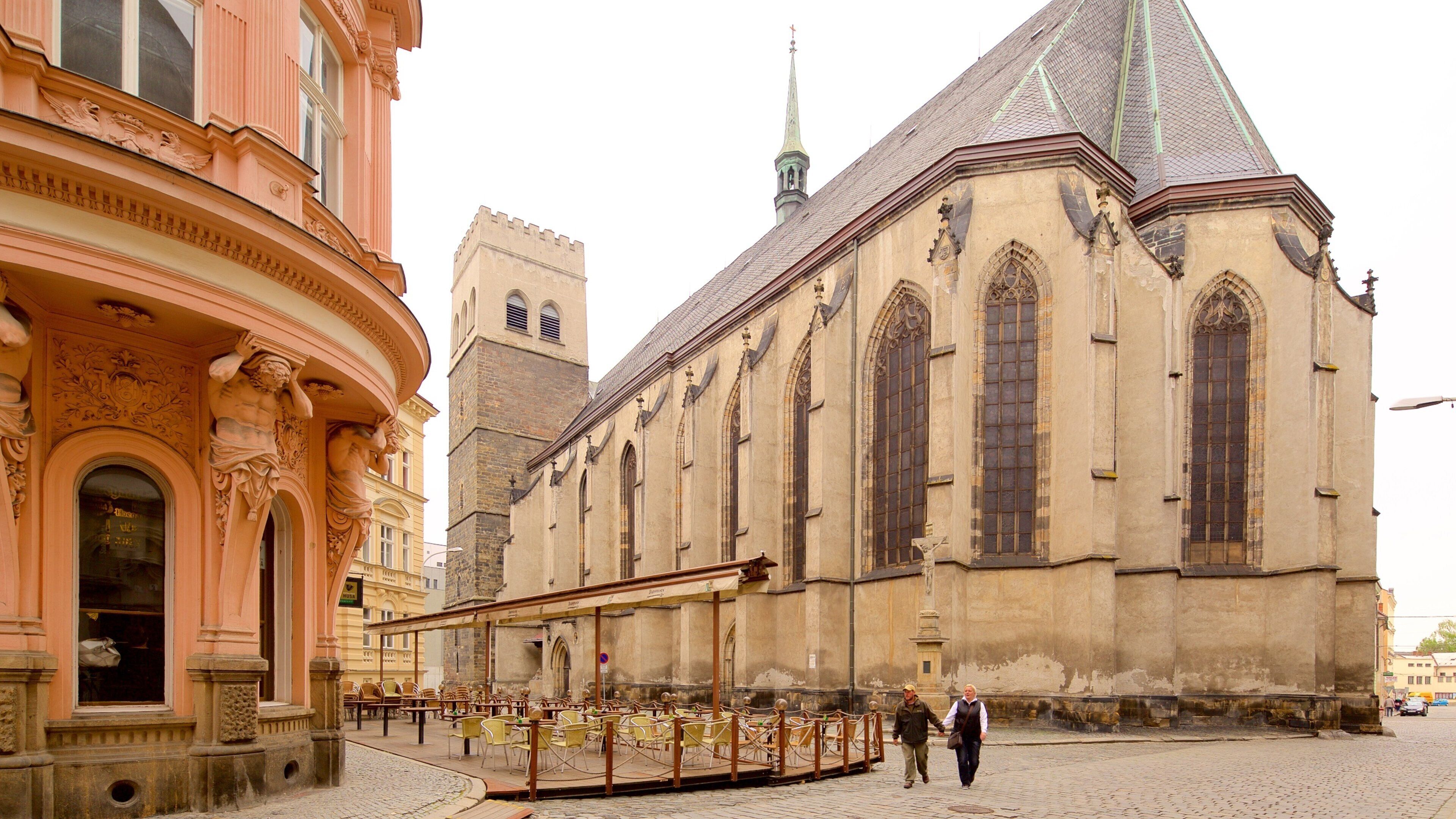 A historic church with Gothic architecture, a clock tower, and a cobblestone street with outdoor seating.