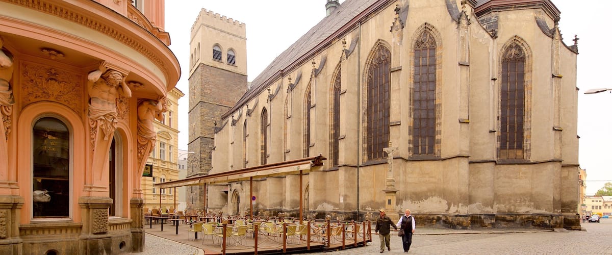 A historic church with Gothic architecture, a clock tower, and a cobblestone street with outdoor seating.
