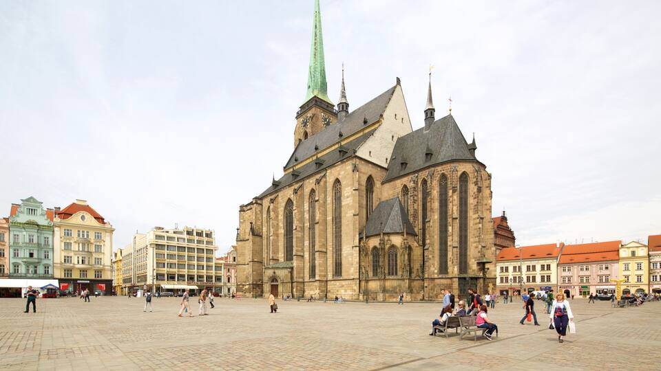 Una iglesia histórica con una aguja alta, rodeada de edificios coloridos y una plaza adoquinada.