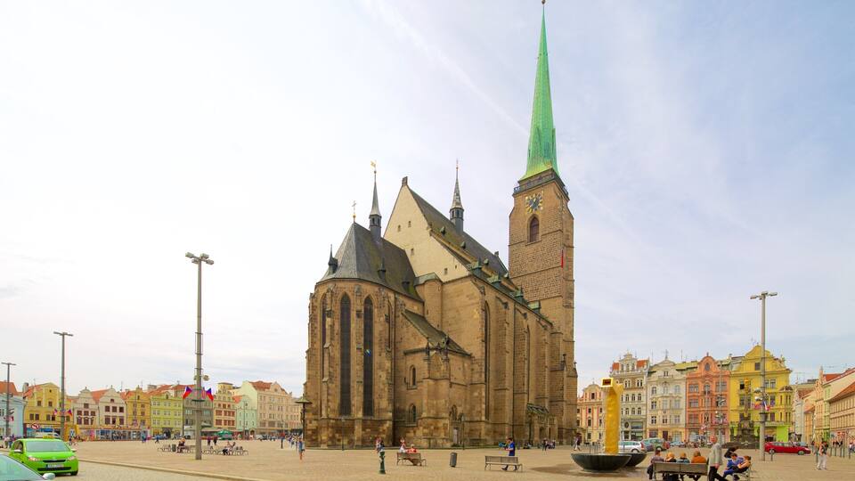 Una iglesia histórica con una aguja alta, rodeada de edificios coloridos y una plaza adoquinada.