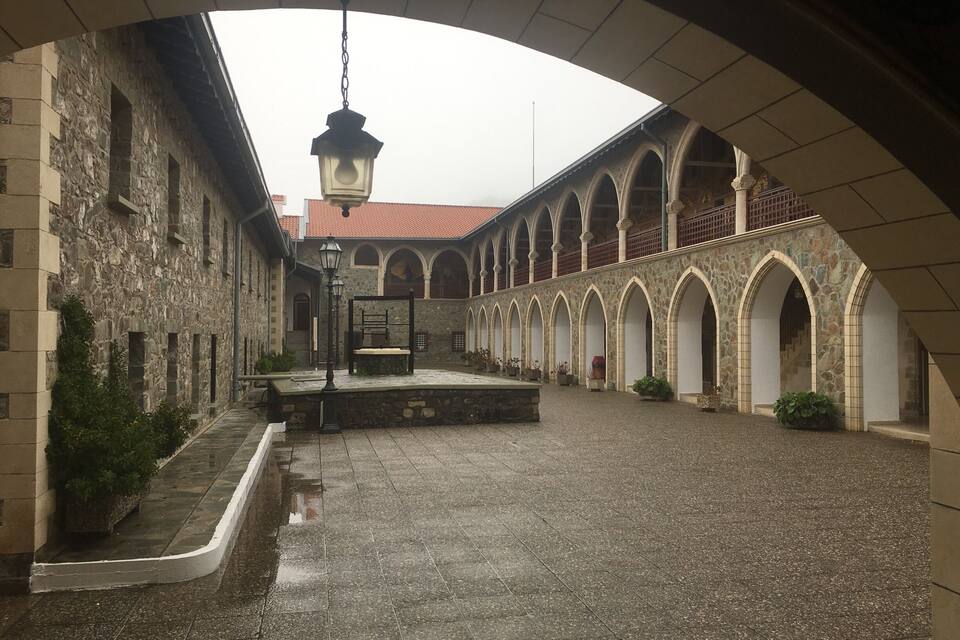 An arched courtyard with stone buildings, a central bench, and a hanging lantern.