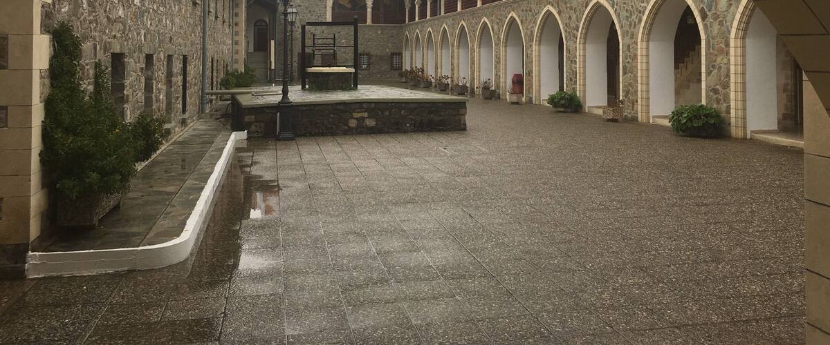 An arched courtyard with stone buildings, a central bench, and a hanging lantern.