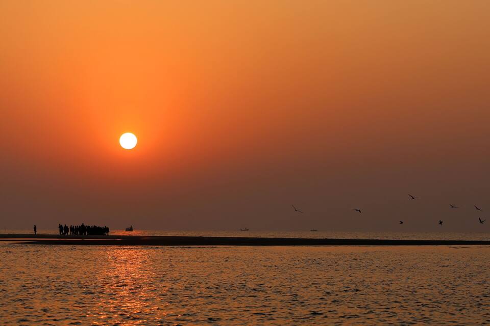 A sunset over a calm sea with a boat and birds flying near the shore.