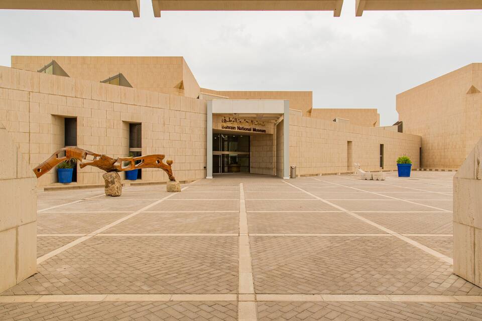 The entrance to the Bahrain National Museum with a wooden sculpture in the foreground.