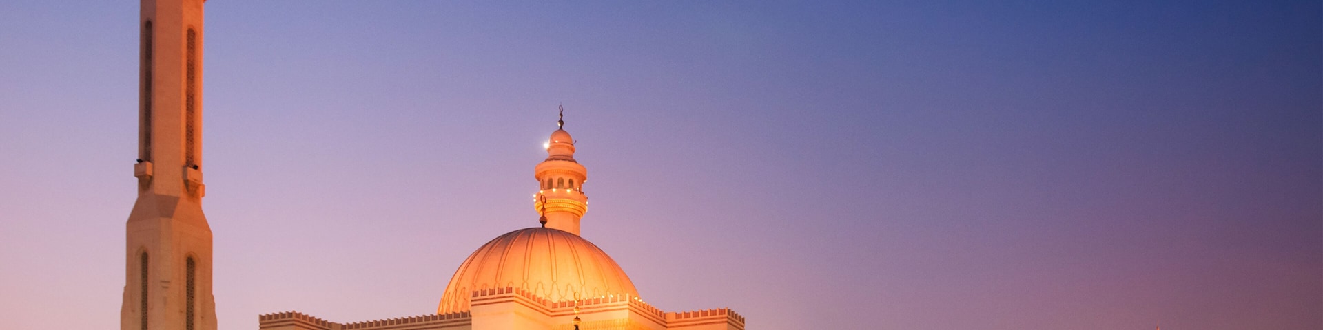 Eine groĂe Moschee mit einem markanten Minarett und einer Kuppel, umgeben von einem weitlĂ€ufigen Innenhof mit SpaziergĂ€ngern.