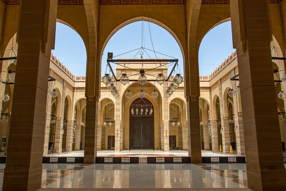 A grand hall with arches, a chandelier, and a large door.