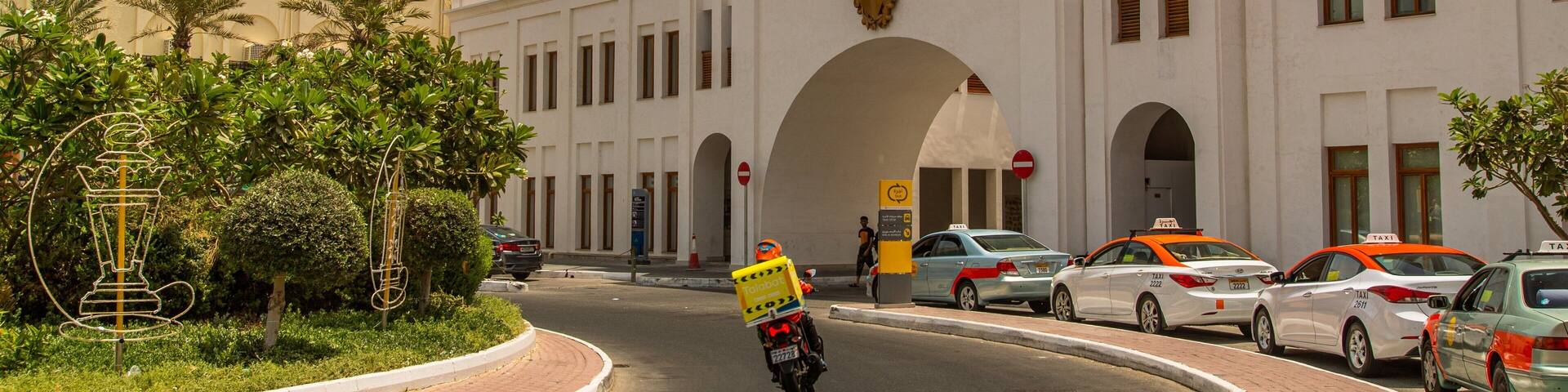 A white building with an arched entrance, a flag, and a taxi sign.