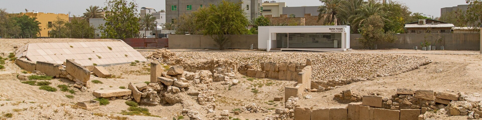 Ancient ruins with stone blocks and a modern visitor center in the background.