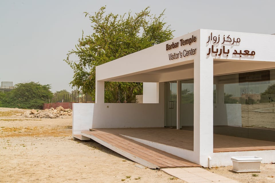 A white visitor center with Arabic signage, a glass door, and a wooden ramp.