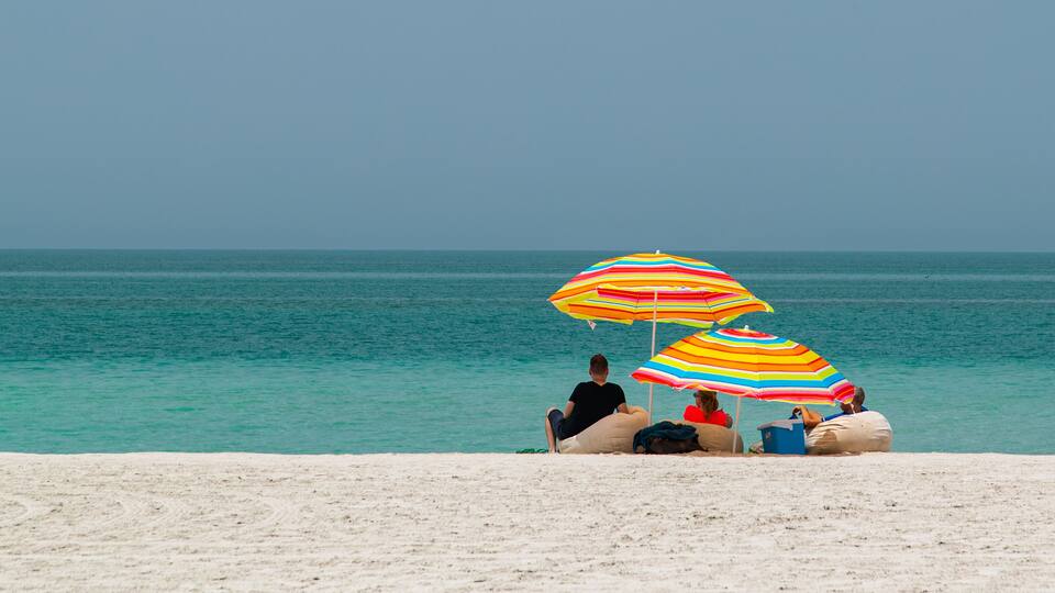 A beach with people sitting under colorful striped umbrellas.