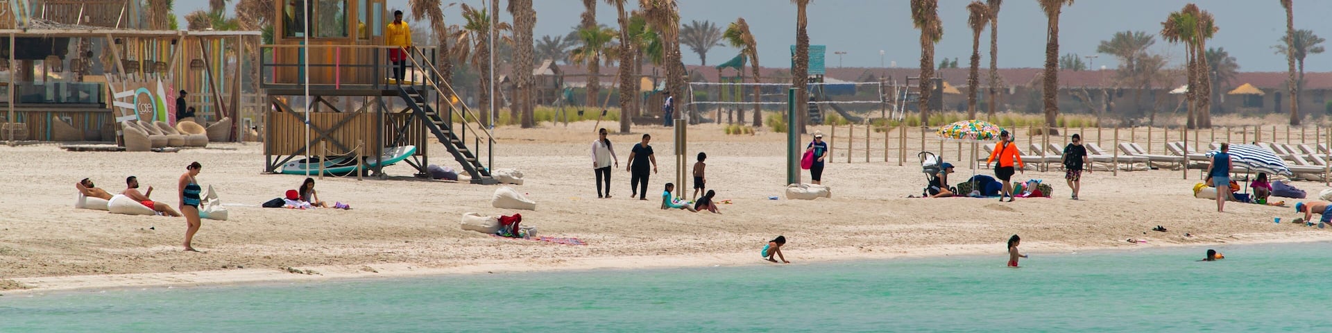 A beach with palm trees, a lifeguard tower, and people relaxing.