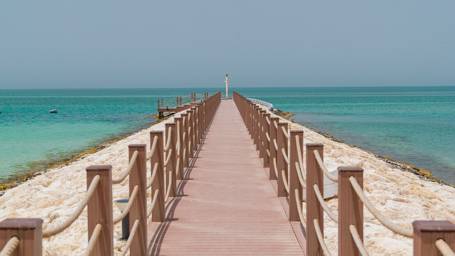 Un muelle de madera que se adentra en un mar turquesa bajo cielos despejados.